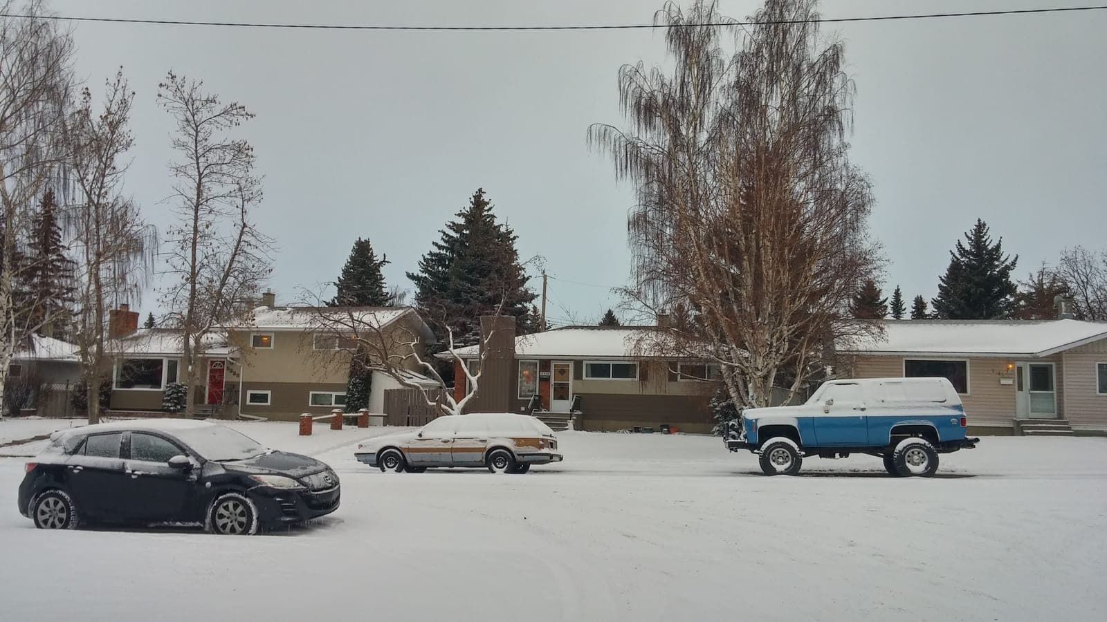 Snow-covered houses along a quiet Calgary residential street in winter.